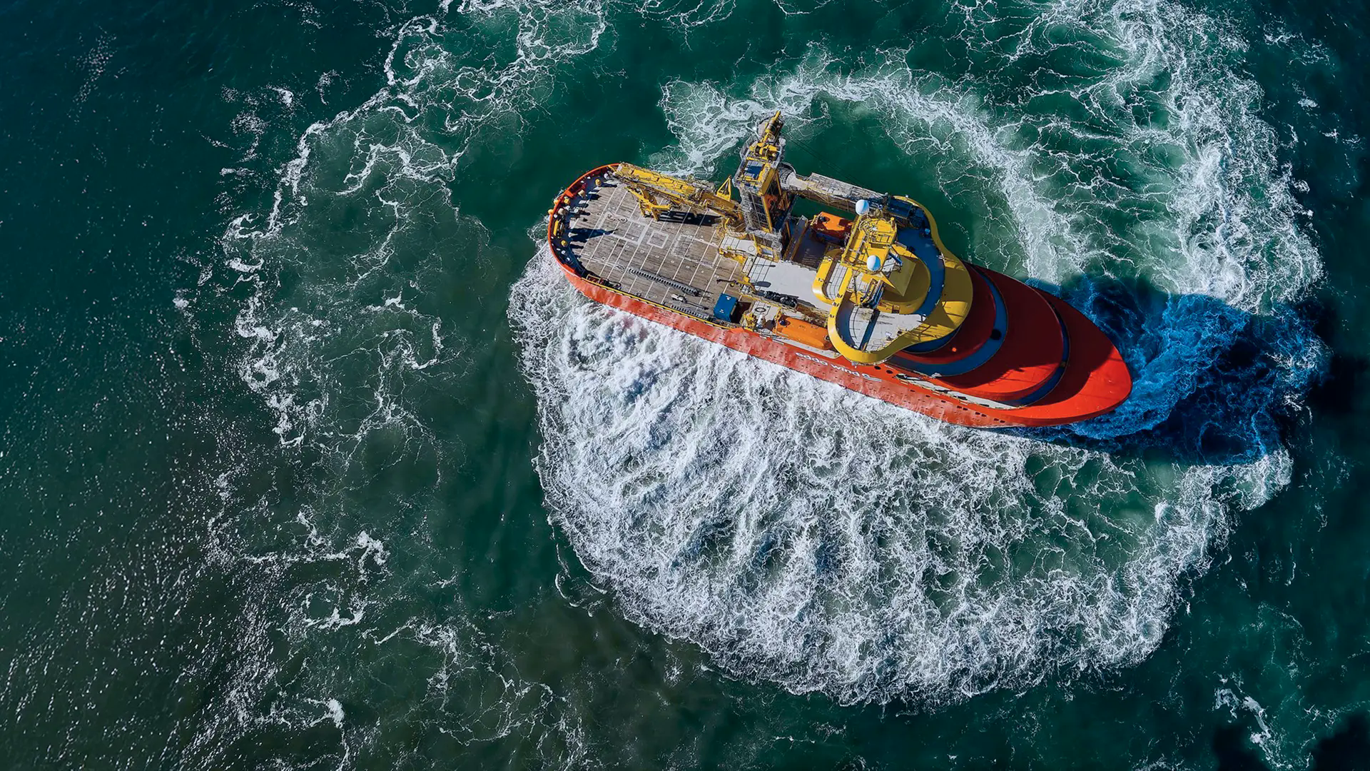 A red work vessel with a deck crane rotates in place; the propulsion creates clearly visible vortices in the water.