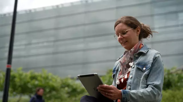 Julia Heinisch sitzt im Freien und arbeitet mit einem Tablet